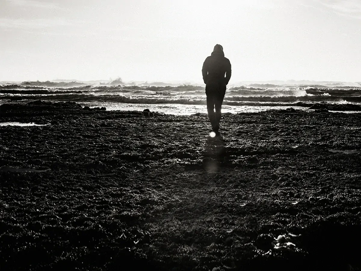 Silhouette van een lopende man tegen een zwart-witte achtergrond van zand en golven. 