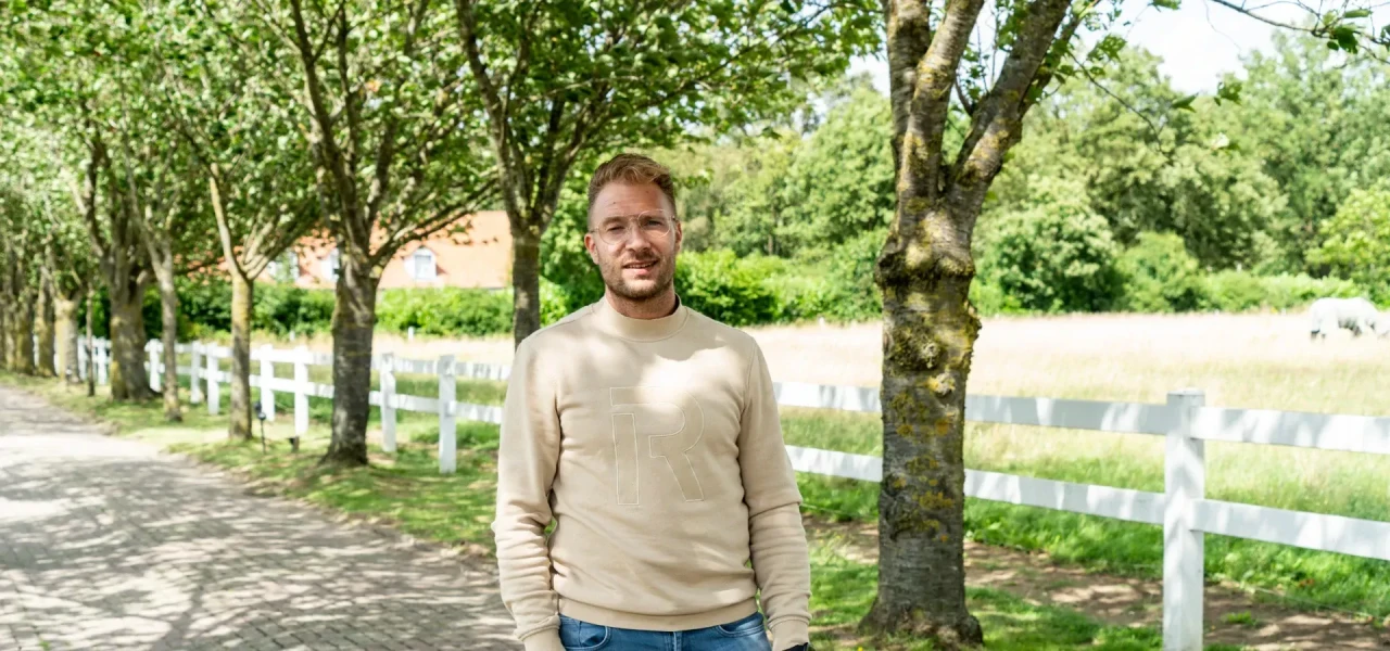 Foto van het herstelverhaal van Rob die op de oprit met groene bomen staat van de afkickkliniek Kortenbos SGGZ Connection.
