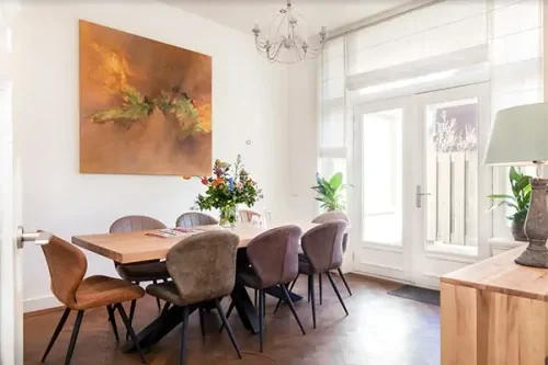 Vergaderruimte met een houten tafel, bruine leren stoelen, een schilderij en witte muren.