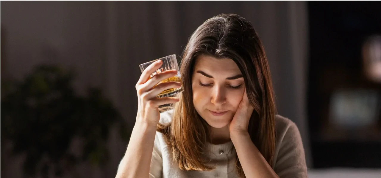 Vrouw met alcoholverslaving heeft een glas drank in haar hand en kijkt naar beneden.
