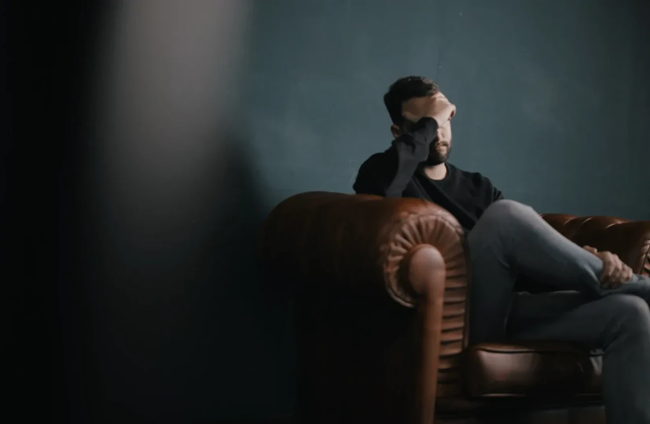 Donkere foto van een depressieve man op bruine bank met het hoofd in de hand. 
