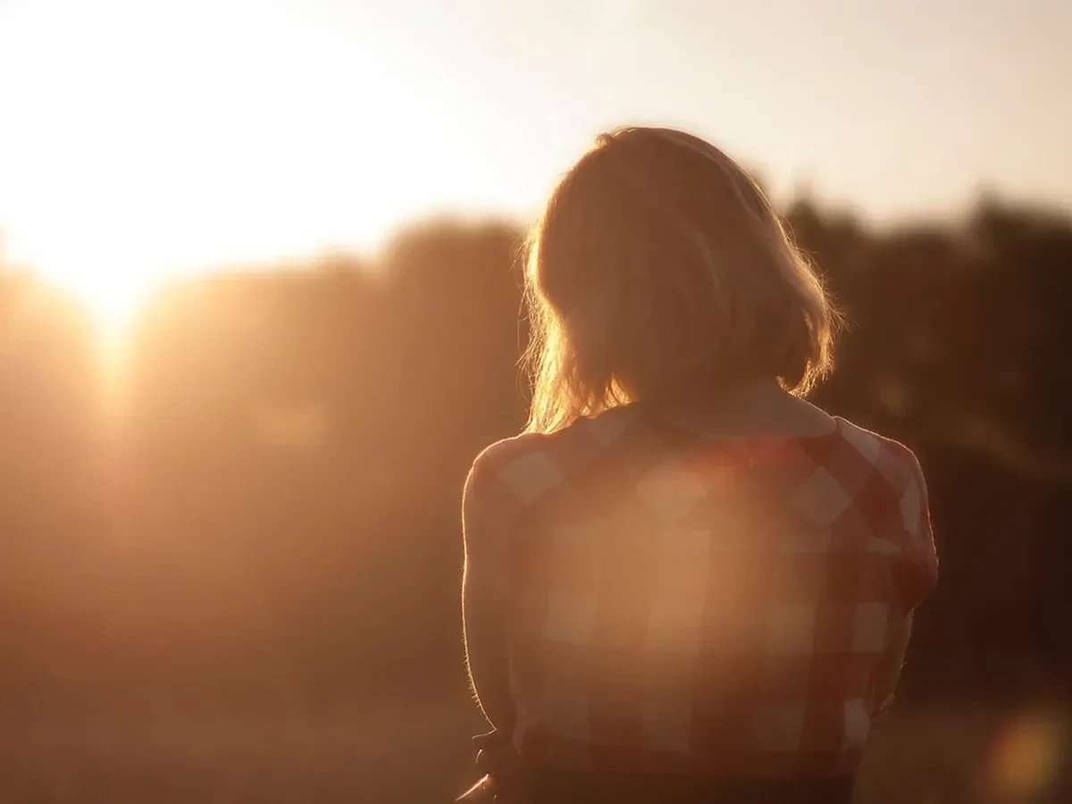 Achteraanzicht van een vrouw in een geruiten shirt die naar de zonsondergang kijkt en met de rug naar de kijker toe staat. 