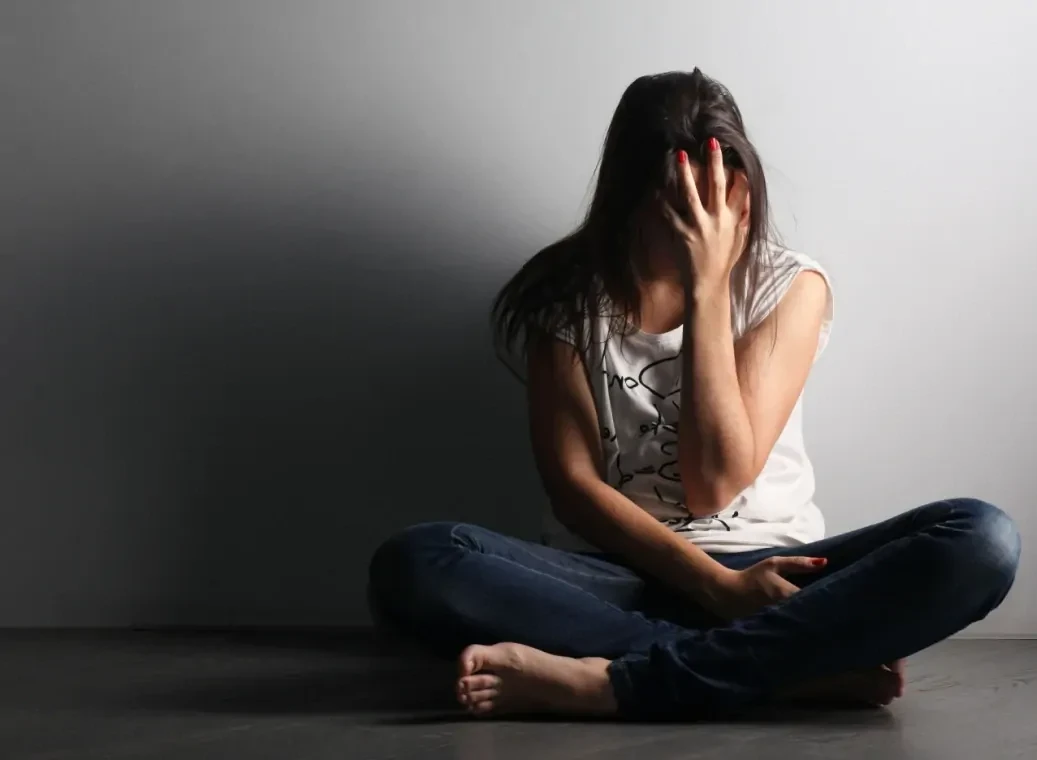 Depressieve vrouw zittend tegen een witte muur met het hoofd in haar hand.