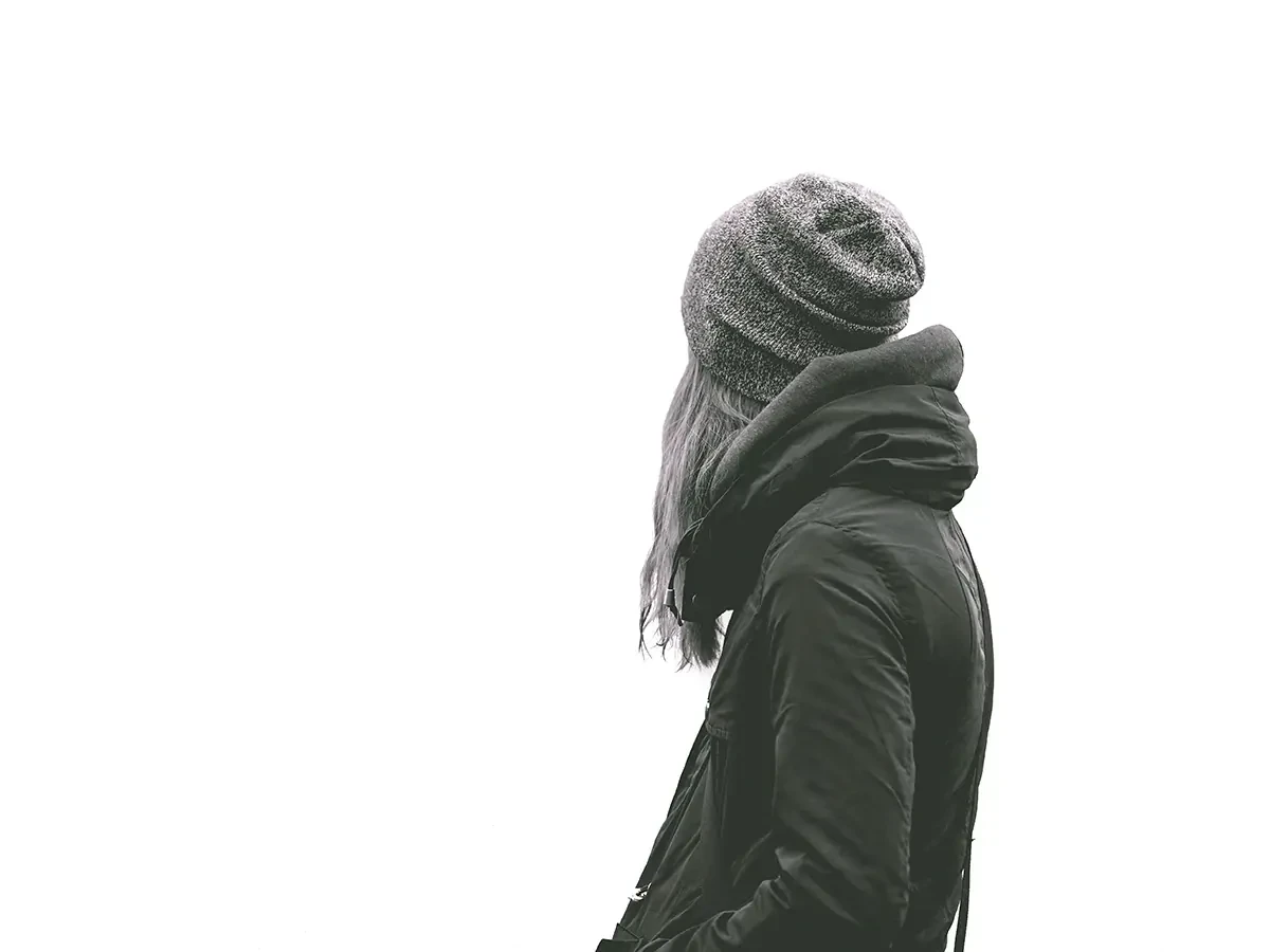 Zwart-wit foto van vrouw in winterjas en muts tegen en volledig witte achtergrond. 