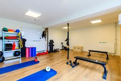 Sportruimte met houten vloer, sportbankjes, yogamatten en gewichten tegen de muur.