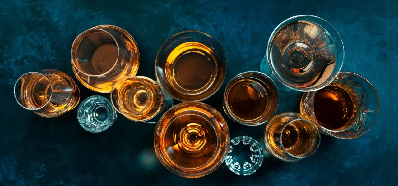 Verschillende glazen met verschillende type alcohol van bovenaf gefotografeerd tegen een blauwe achtergrond.