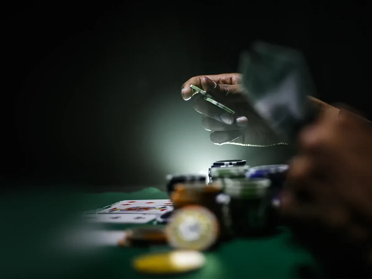De handen van iemand met een gokverslaving die met fiches en kaarten aan het gokken is tegen een donkergroene achtergrond. 