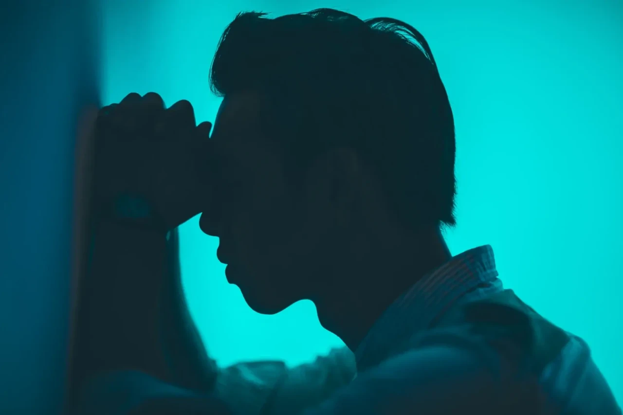 Silhouette van man leunend met zijn hoofd op zijn handen tegen de muur met een felblauwe achtergrond.