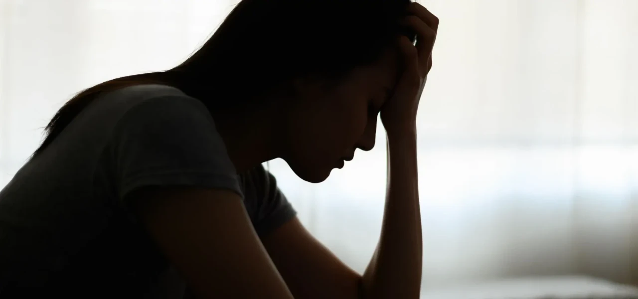 Silhouette van een depressieve vrouw met het hoofd in haar hand tegen een lichte achtergrond.  