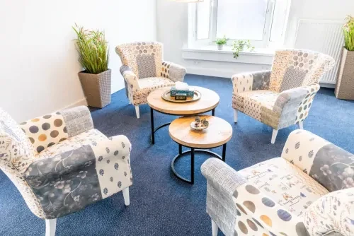 Behandelkamer met twee kleine salontafels, 4 bedrukte stoelen in een kringopstelling op een blauw tapijt.